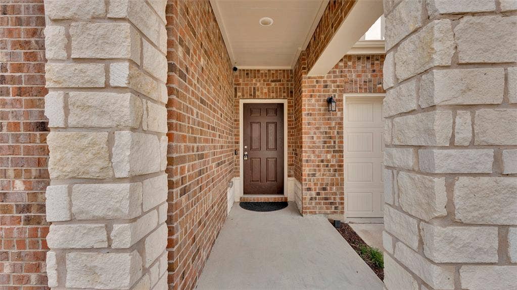 707 Indigo Road, Princeton, TX 75407 Exterior facade featuring a brown paneled entry door, light brick, stacked stone accents, and a panel-style garage door
