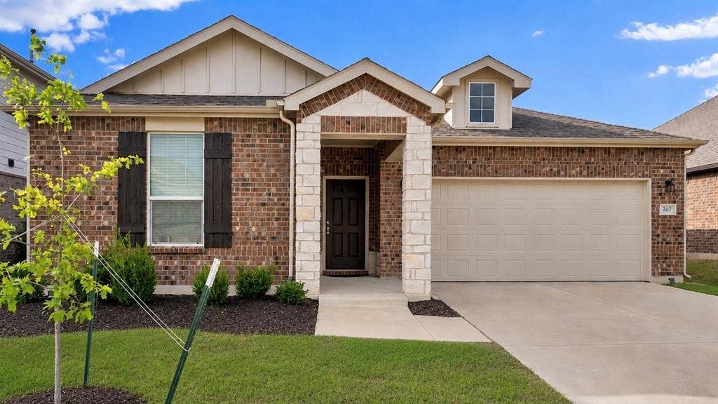 707 Indigo Road, Princeton, TX 75407 Brick and stone exterior featuring a covered entry, an attached two-car garage, manicured shrubs, and a concrete driveway