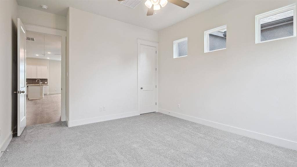Carpeted room with ceiling fan, white walls, and three upper windows