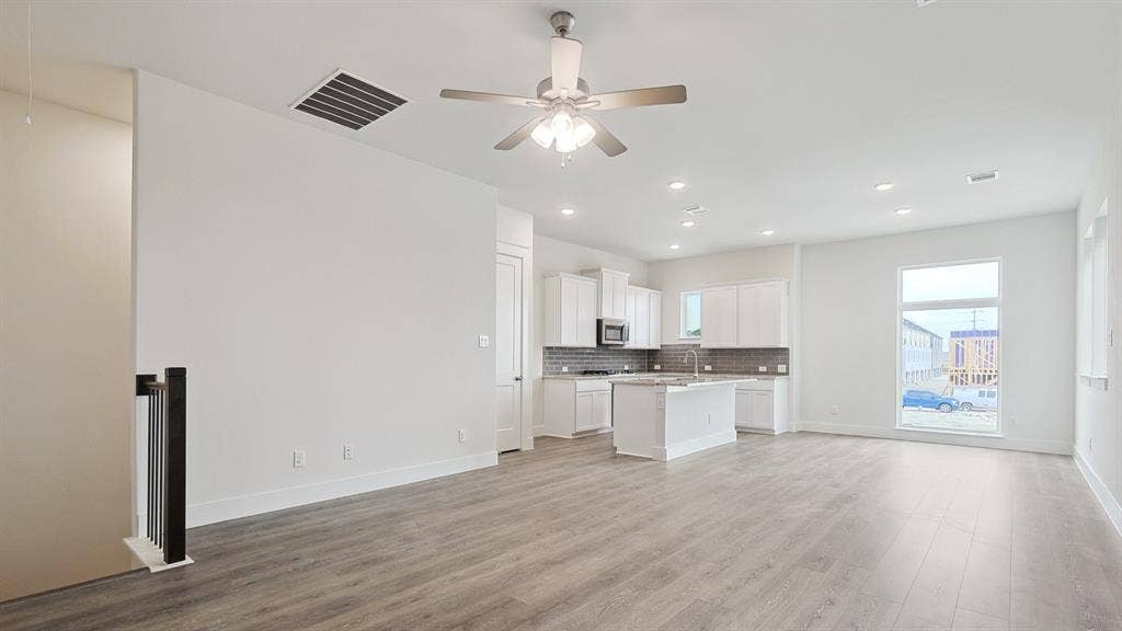 Open concept living space featuring wood-finish flooring, white walls, and a modern ceiling fan with integrated lighting