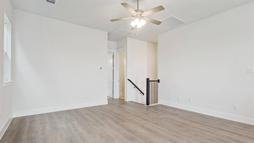 Spacious room featuring wood-finish flooring, a ceiling fan, and white baseboards