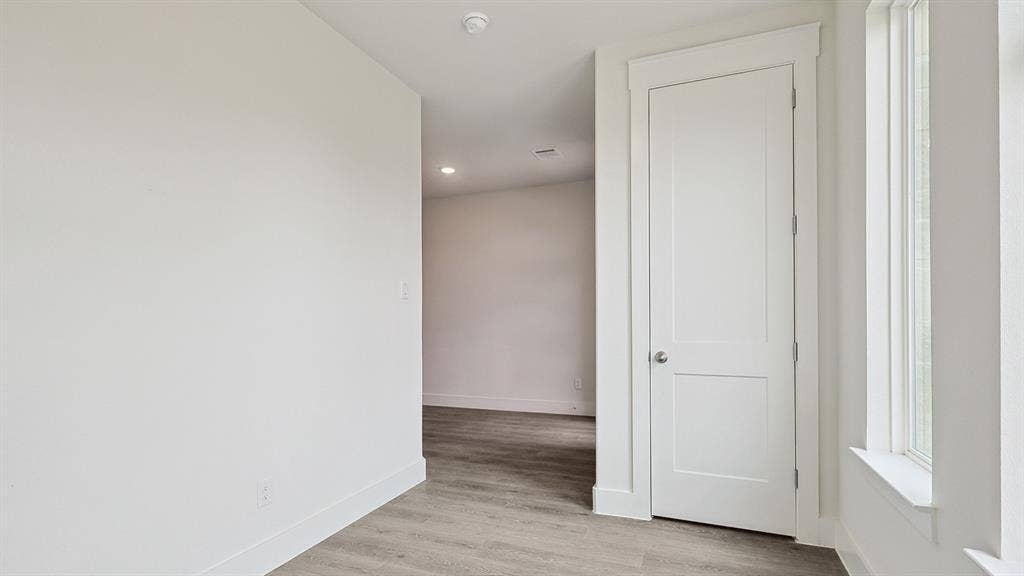 Light-filled interior space featuring wood-finish flooring, white trim, recessed lighting, and a two-panel door