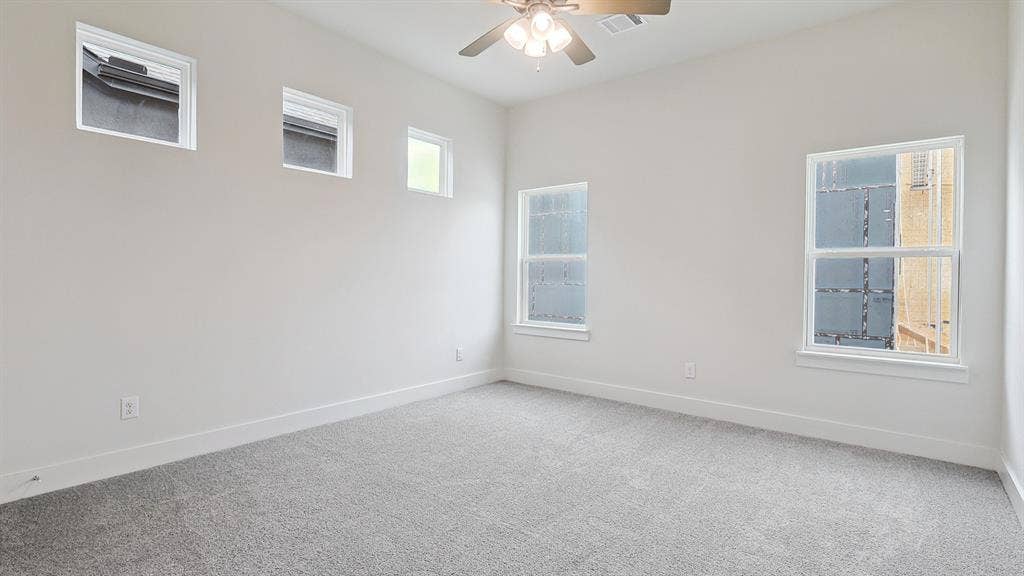 Spacious room featuring light gray carpeting, multiple windows, high ceilings, and a ceiling fan with integrated lighting