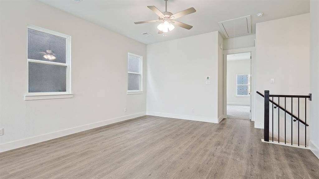 Spacious room with wood-finish flooring, two windows, and a ceiling fan