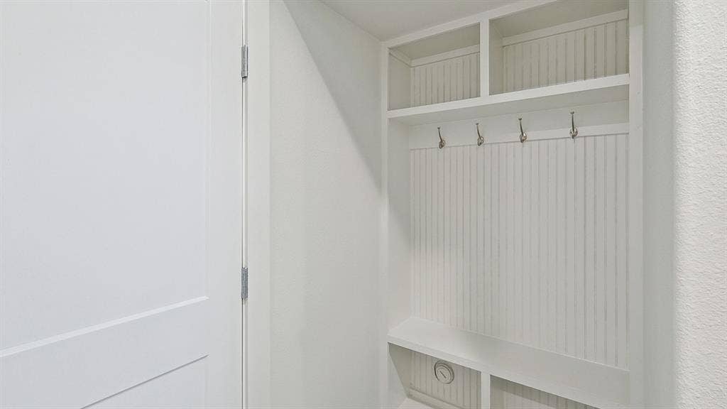 Built-in mudroom station featuring beadboard backing, four metal hooks, open shelving, and lower cubbies