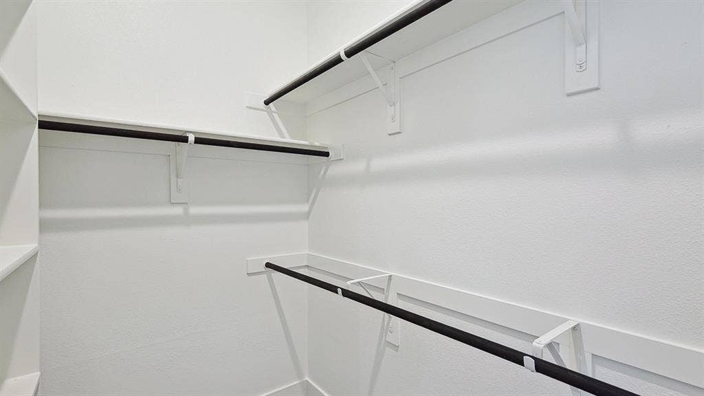 Walk-in closet featuring white walls, integrated shelving, and multiple hanging rods