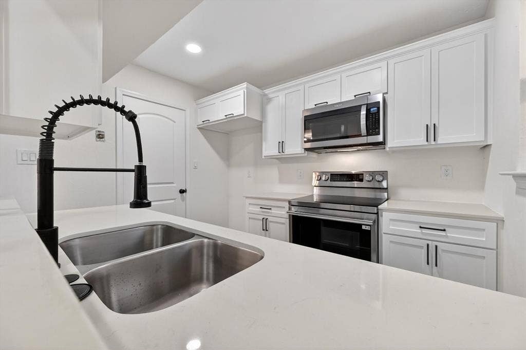 428 Dollins Street, Cedar Hill, TX 75104 Kitchen featuring white cabinetry, light-toned countertops, a stainless steel double basin sink with a matte black pull-down faucet, stainless steel range, and an over-the-range microwave