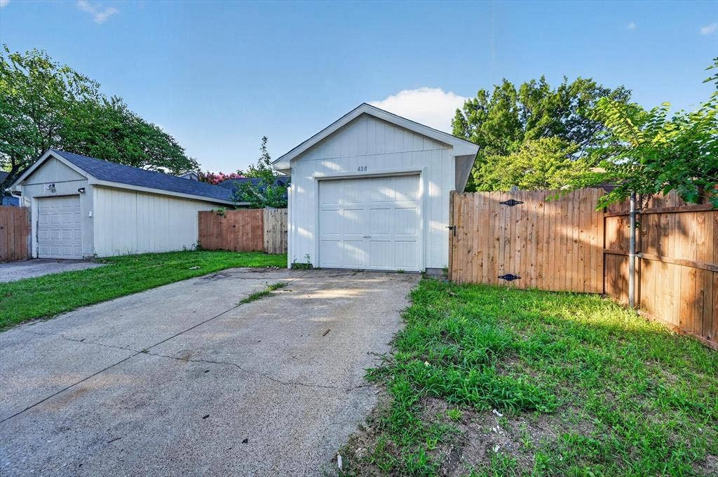 428 Dollins Street, Cedar Hill, TX 75104 Two detached garages with white garage doors, a concrete driveway, a wood fence with black hardware, and green grass patches
