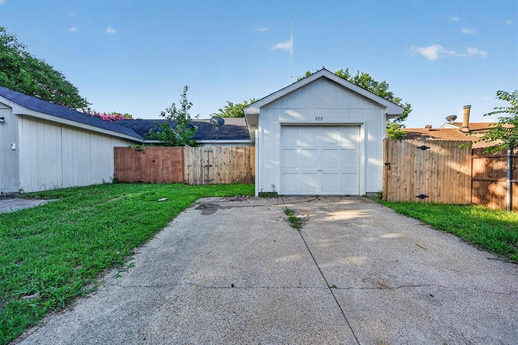428 Dollins Street, Cedar Hill, TX 75104 Detached garage structure with a white panel door, concrete driveway, and surrounding wood fencing