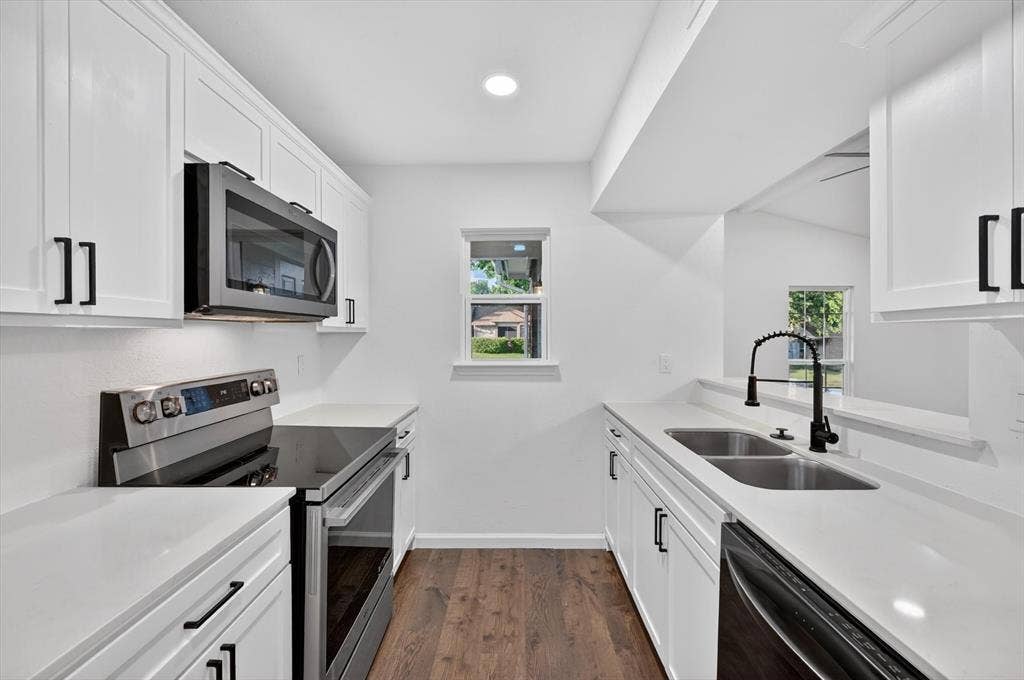 428 Dollins Street, Cedar Hill, TX 75104 Modern kitchen featuring white shaker cabinetry, stainless steel appliances, solid surface countertops, a matte black gooseneck faucet, and wood-finish flooring