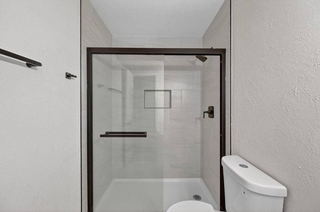428 Dollins Street, Cedar Hill, TX 75104 Enclosed shower with dark-framed glass doors, white tiled interior, a built-in shower niche, and a contrasting dark-finish showerhead