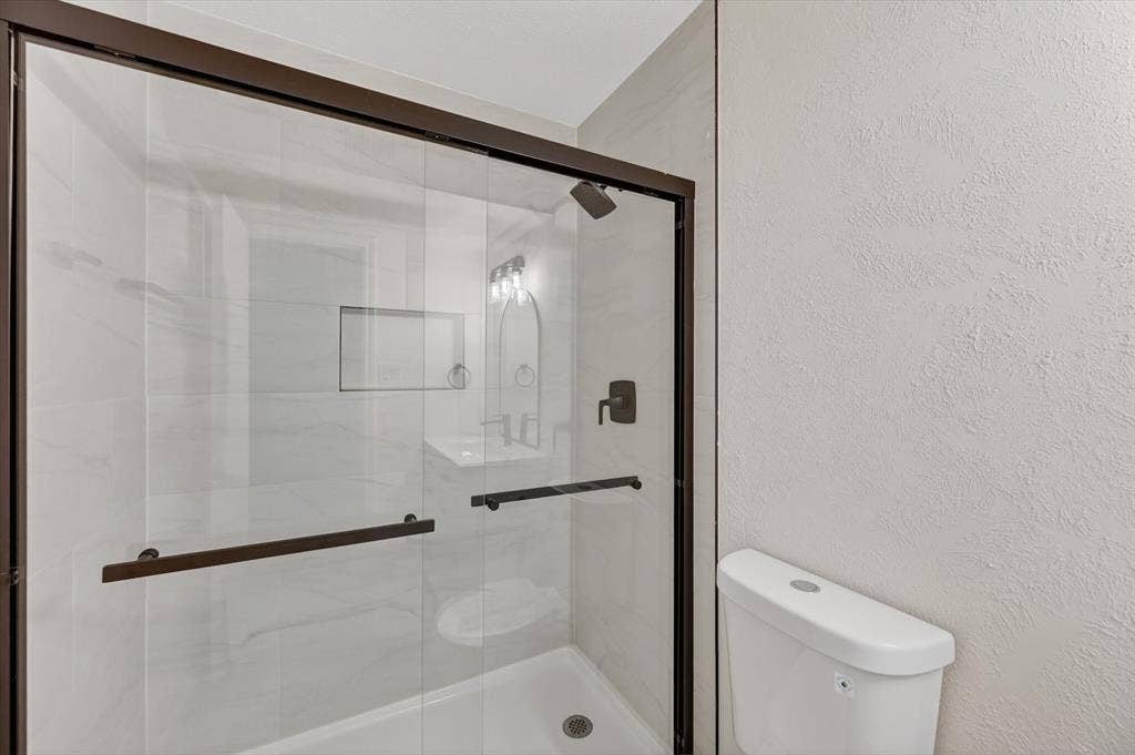 428 Dollins Street, Cedar Hill, TX 75104 Glass-enclosed shower with dark bronze framing and hardware, featuring white tiled walls, a built-in shower niche, and a white shower base