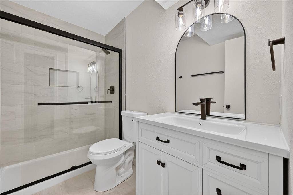 428 Dollins Street, Cedar Hill, TX 75104 Bathroom featuring a white vanity with integrated sink, black hardware, arched mirror, and multi-bulb vanity light
