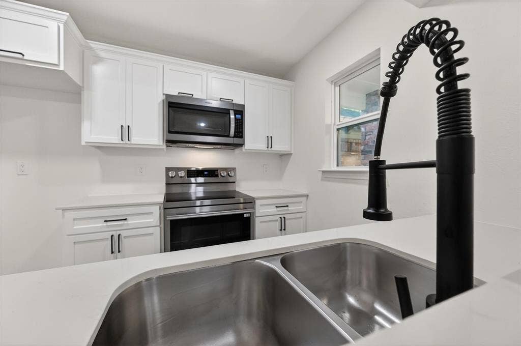 428 Dollins Street, Cedar Hill, TX 75104 Modern kitchen featuring white cabinetry with dark pulls, stainless steel appliances, white countertops, and a dual basin sink with a matte black pull-down faucet