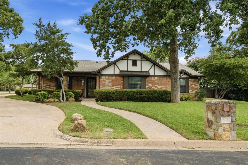 521 W Louella Drive, Hurst, TX 76054 Well maintained home with lush green grass, mature trees, and a long driveway.