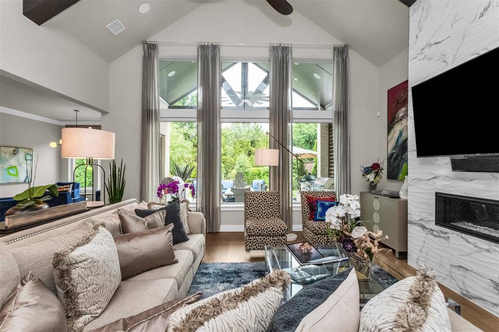 8138 Edgefield Court, Frisco, TX 75035 Vaulted ceiling living area featuring a linear gas fireplace with a marble-finish surround, wood-finish flooring, and expansive windows