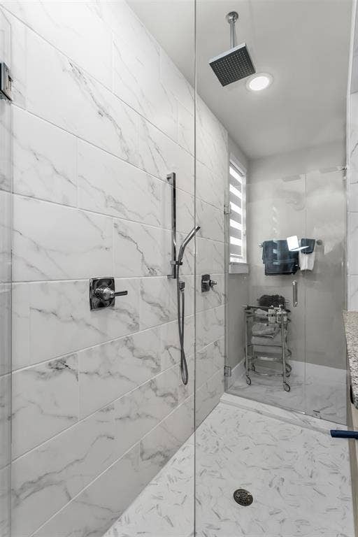 8138 Edgefield Court, Frisco, TX 75035 Glass-enclosed shower featuring large format wall tiles, a rain showerhead, a handheld shower fixture, and a mosaic tiled floor