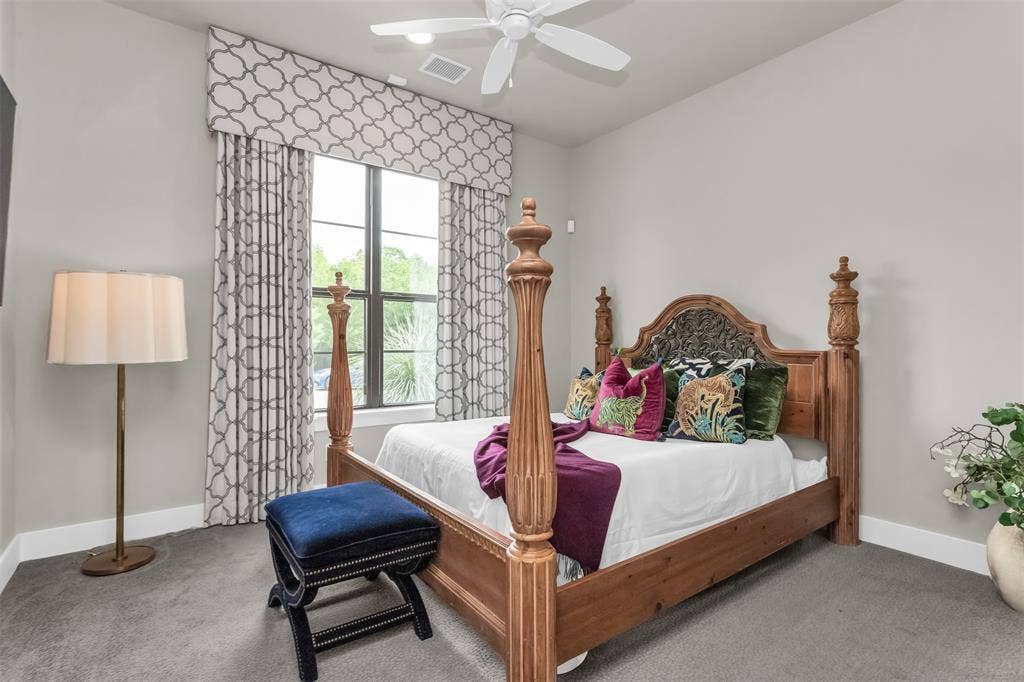 8138 Edgefield Court, Frisco, TX 75035 Carpeted bedroom featuring a ceiling fan with integrated lighting, a large window with patterned drapes, light gray wall paint, and white baseboards
