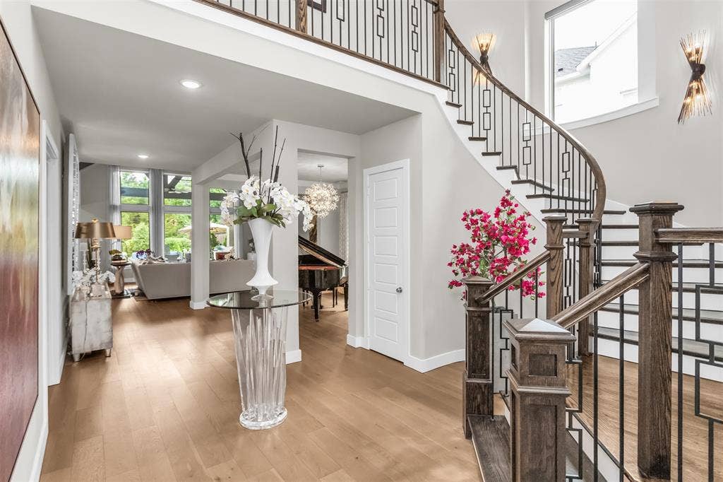 8138 Edgefield Court, Frisco, TX 75035 Gracious entry foyer featuring light wood-finish flooring, a grand curved staircase with dark wood newel posts and iron balusters, and elegant wall sconces