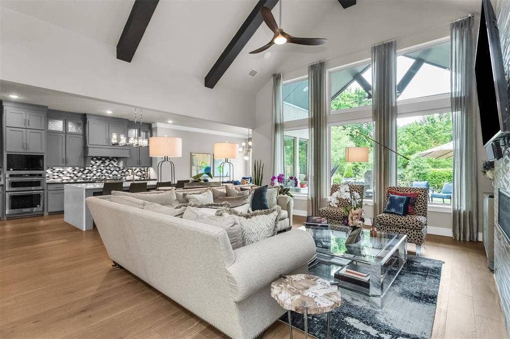 8138 Edgefield Court, Frisco, TX 75035 Open-concept living area featuring a vaulted ceiling with exposed beams, wood-finish flooring, and a wall of tall windows