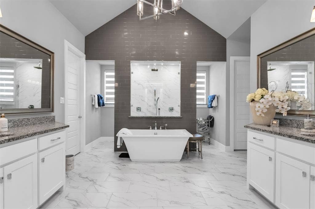 8138 Edgefield Court, Frisco, TX 75035 Freestanding soaking tub with dual showers, set against a dark gray subway tile accent wall and white marble-look flooring