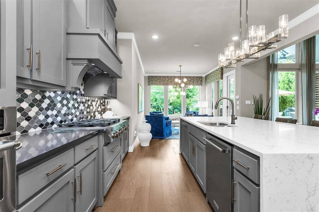 8138 Edgefield Court, Frisco, TX 75035 Gourmet kitchen featuring grey cabinetry, stainless steel range with custom hood, mosaic tile backsplash, spacious center island with sink, and wood-finish flooring