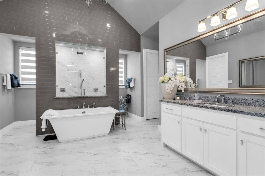 8138 Edgefield Court, Frisco, TX 75035 Spacious bathroom featuring a freestanding tub, expansive walk-in shower with glass enclosure, dual vanity with undermount sinks and stone countertop, large wall-mounted mirror, and tile flooring
