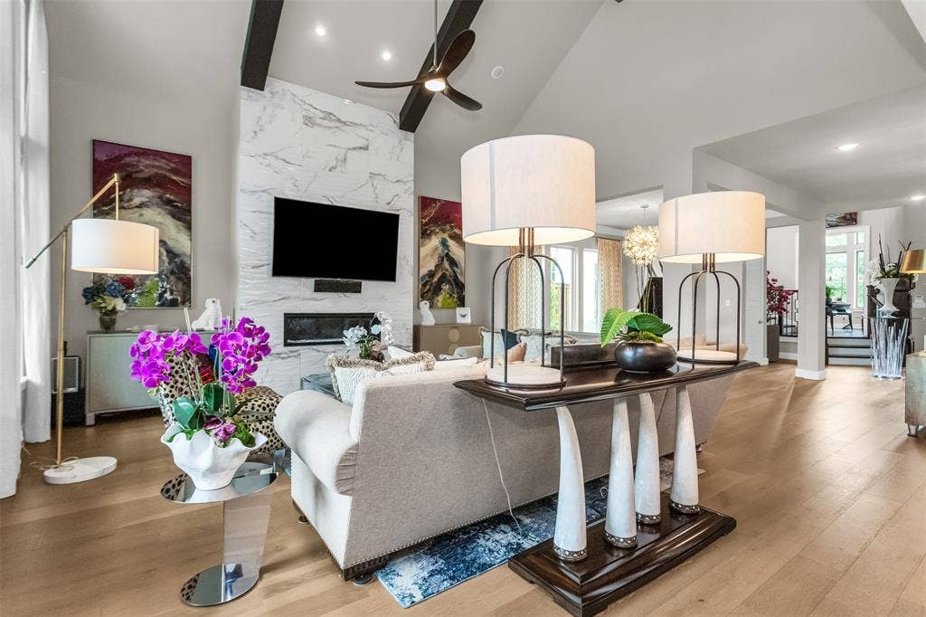 8138 Edgefield Court, Frisco, TX 75035 Vaulted ceiling living space featuring a floor-to-ceiling fireplace with an integrated television, exposed ceiling beams, a ceiling fan, and wood-finish flooring