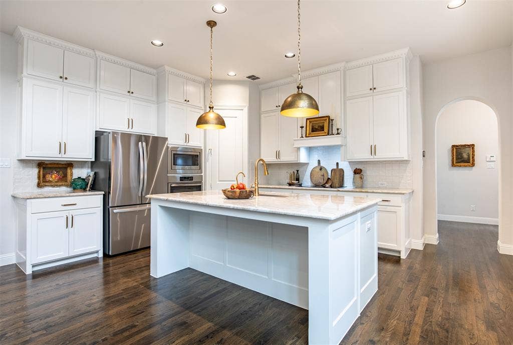7405 Collin Mckinney Parkway, McKinney, TX 75070 Open-concept kitchen featuring a large central island with Taj Mahal quartzite countertops, white cabinetry with crown molding, stainless steel appliances