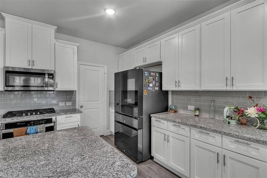 3708 Jan Camille Court, Celina, TX 75009 Kitchen with hardwood / wood-style floors, tasteful backsplash, light stone counters, appliances with stainless steel finishes, and white cabinets