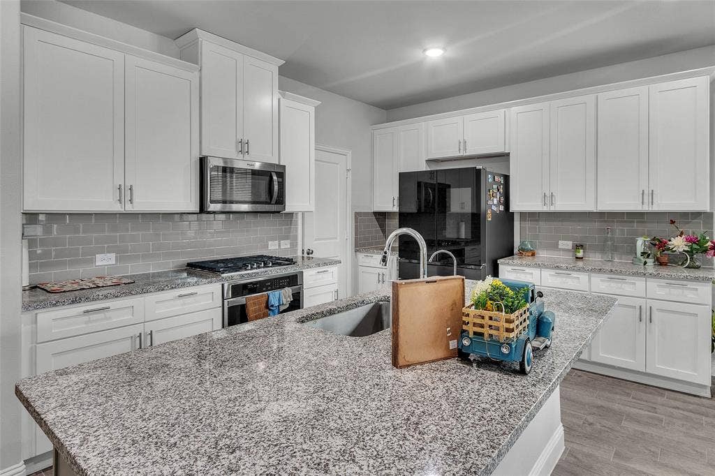 3708 Jan Camille Court, Celina, TX 75009 Kitchen with light wood-type flooring, tasteful backsplash, stainless steel appliances, and white cabinetry