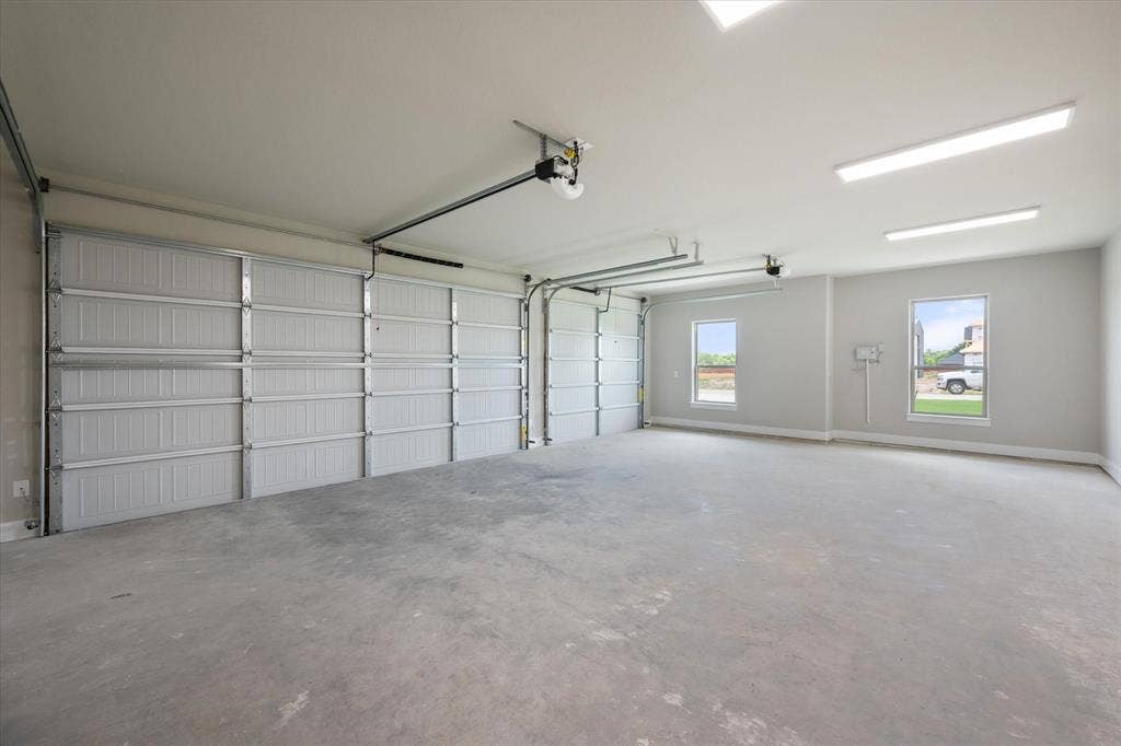 6610 Waggoner Way, Midlothian, TX 76065 Spacious 3-car garage featuring two overhead doors, concrete flooring, overhead fluorescent lighting, and two windows providing exterior visibility