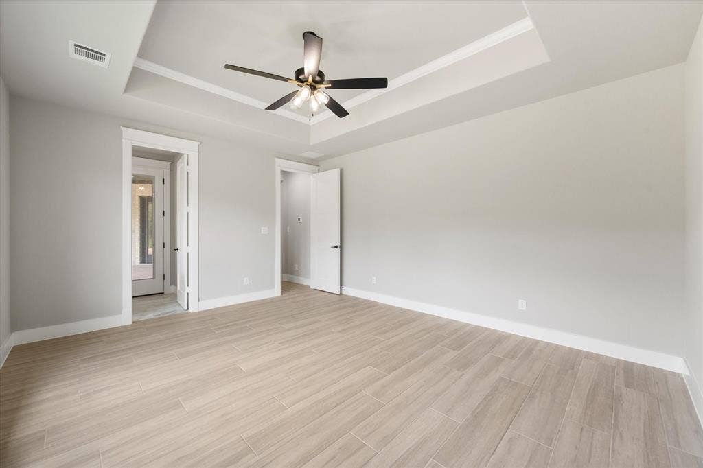 6610 Waggoner Way, Midlothian, TX 76065 Spacious interior featuring wood-look tile flooring, light gray walls, a tray ceiling with crown molding, and a modern ceiling fan