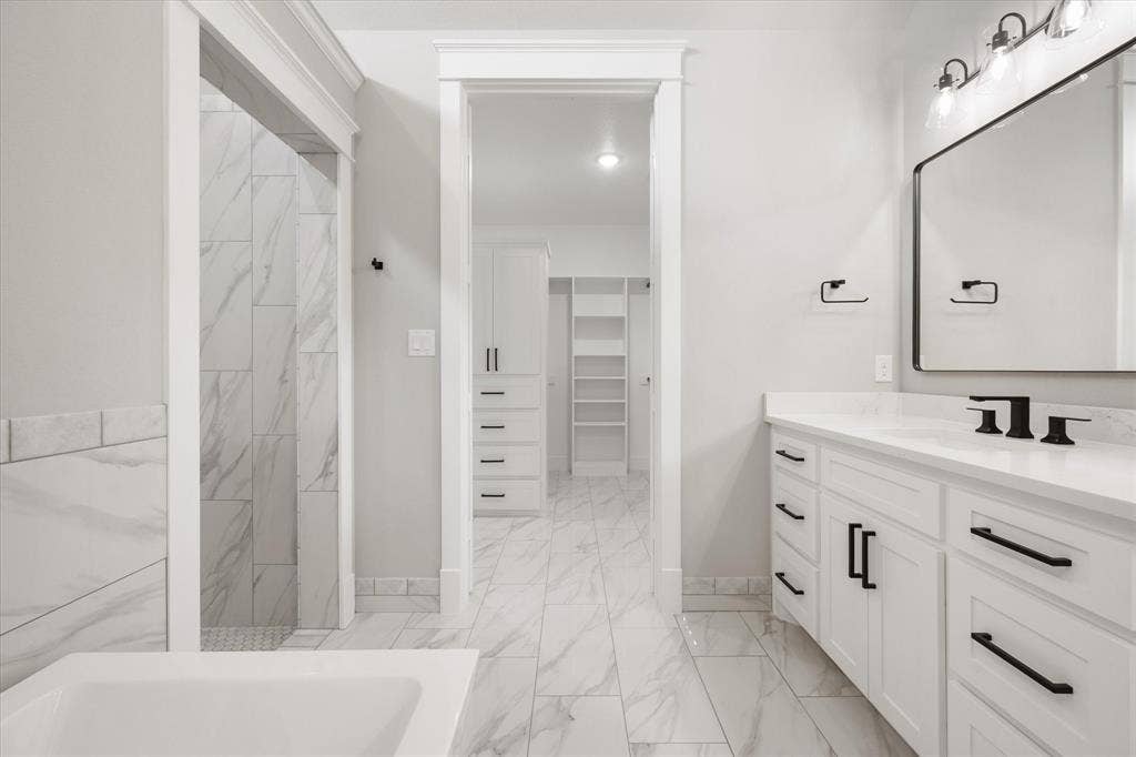 6610 Waggoner Way, Midlothian, TX 76065 Spacious bathroom featuring a double vanity with white cabinetry and black hardware, a large rectangular mirror with black frame, and a tub with marble-look tile surround
