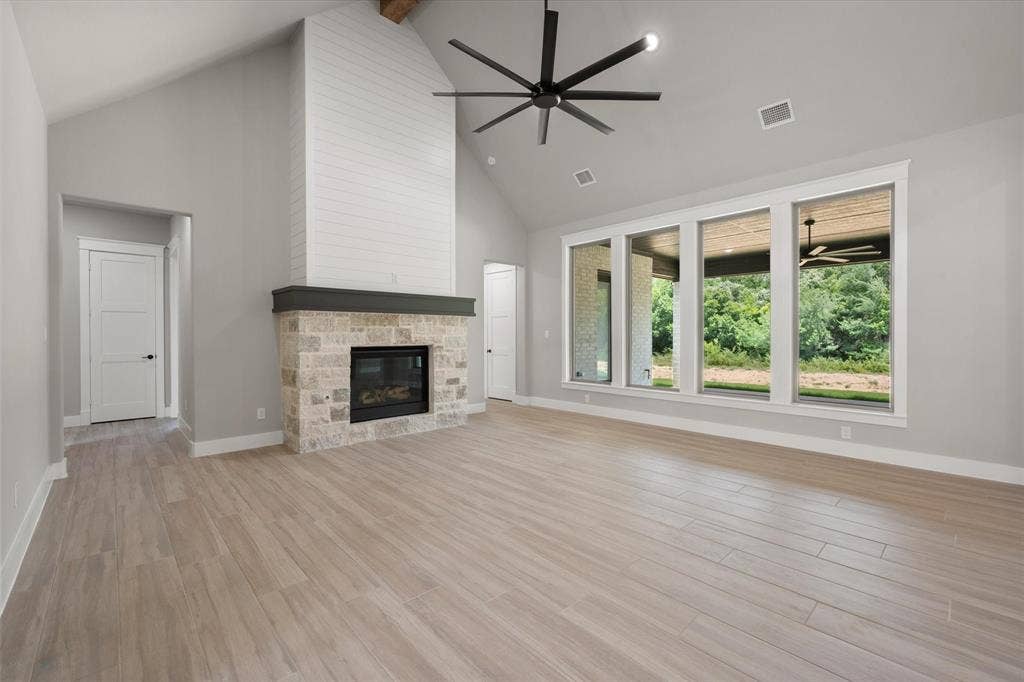6610 Waggoner Way, Midlothian, TX 76065 Spacious living area featuring a vaulted ceiling, wood-finish flooring, and a stone fireplace with a shiplap surround