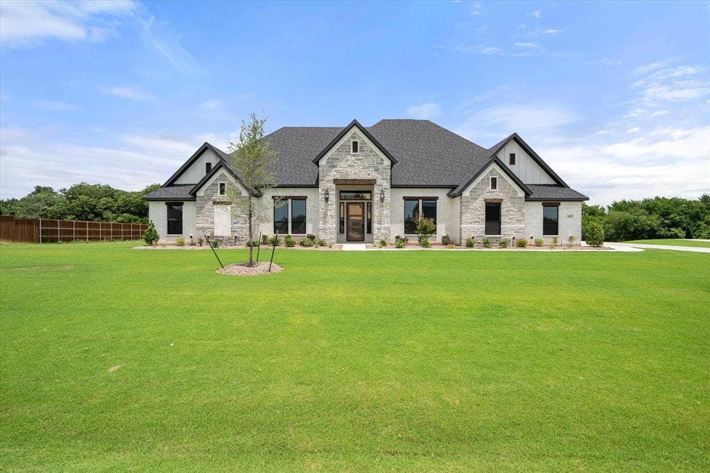 6610 Waggoner Way, Midlothian, TX 76065 Contemporary single-story residence featuring a stone and board-and-batten facade, dark shingle roofing, and multiple large windows