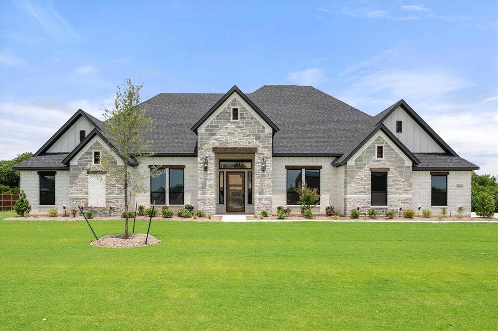 6610 Waggoner Way, Midlothian, TX 76065 Modern farmhouse-style exterior featuring a striking combination of light-colored brick and stone, dark-trimmed windows, a multi-gabled dark shingle roof, vertical white siding accents, and a prominent wood-paneled entry door