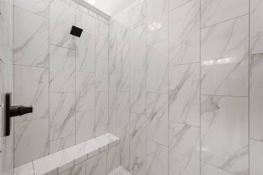 6610 Waggoner Way, Midlothian, TX 76065 Shower enclosure featuring floor-to-ceiling white marble-look tile, a built-in bench, matte black showerhead, and matte black lever handle