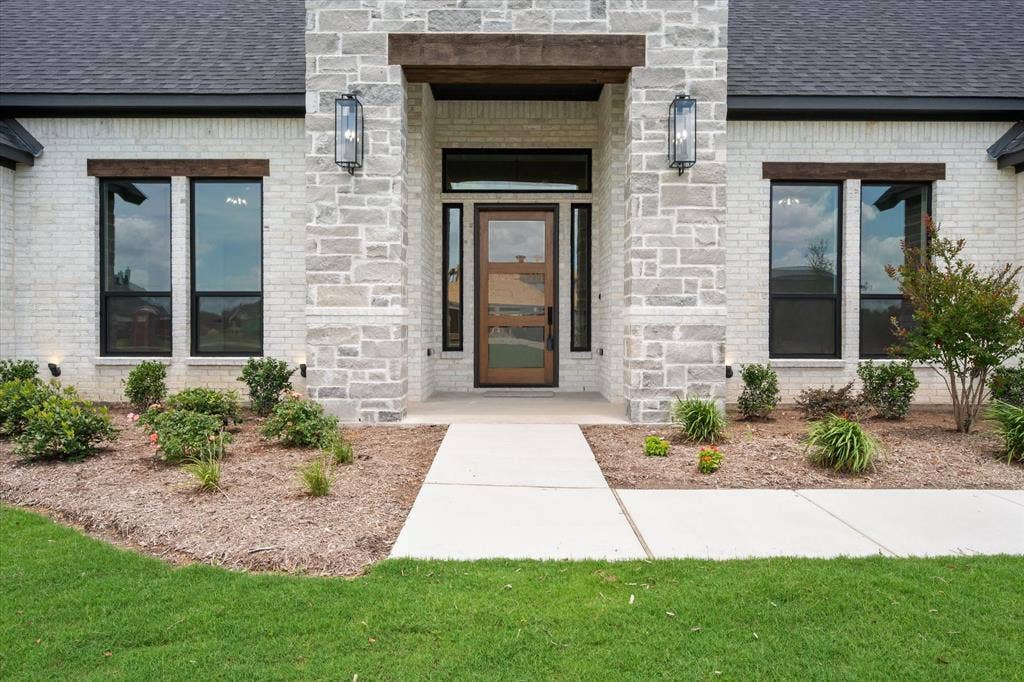 6610 Waggoner Way, Midlothian, TX 76065 Modern facade featuring a wooden entry door with frosted glass panels, surrounded by a light-toned brick and stone veneer