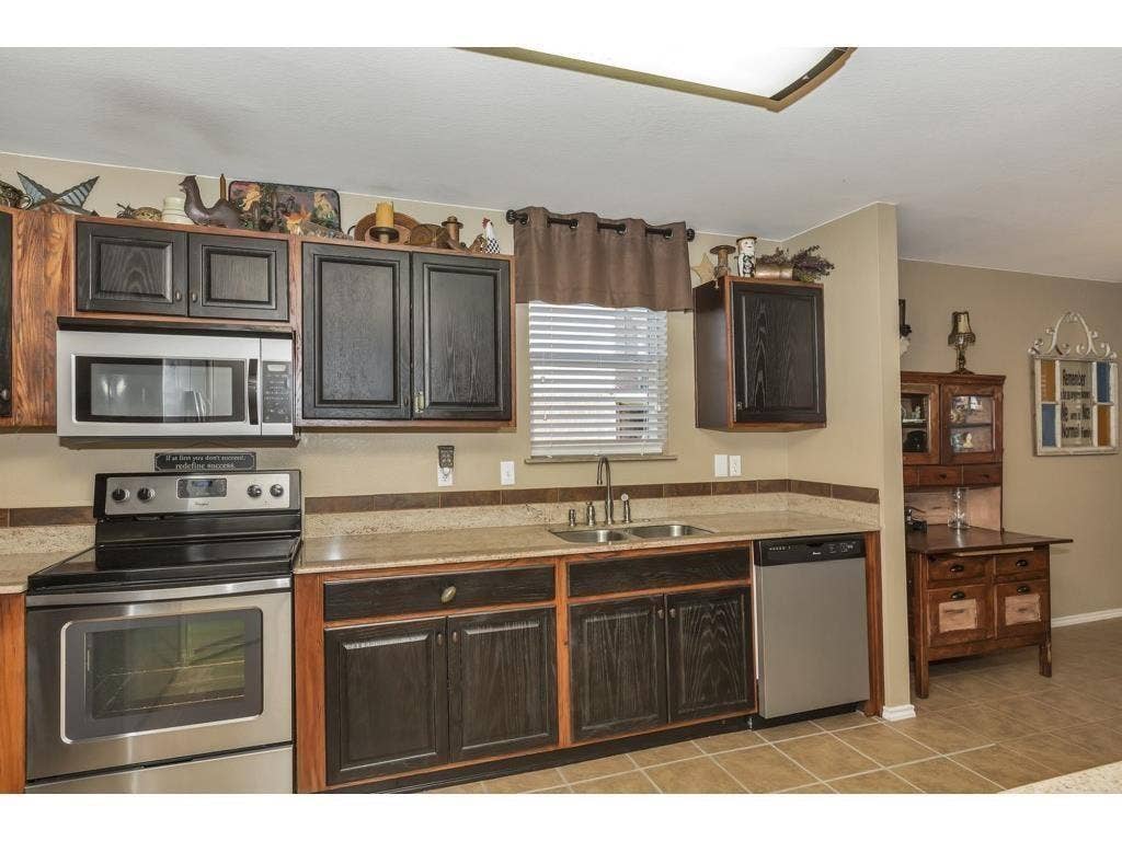 2912 Lake Terrace Drive, Wylie, TX 75098 Kitchen featuring wood-finish cabinetry, stainless steel appliances, a double basin sink, light-toned countertops, and tile flooring
