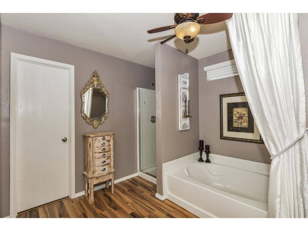 2912 Lake Terrace Drive, Wylie, TX 75098 Bathroom featuring a built-in soaking tub, glass-enclosed shower, wood-finish flooring, ceiling fan with light fixture, and a window with blinds