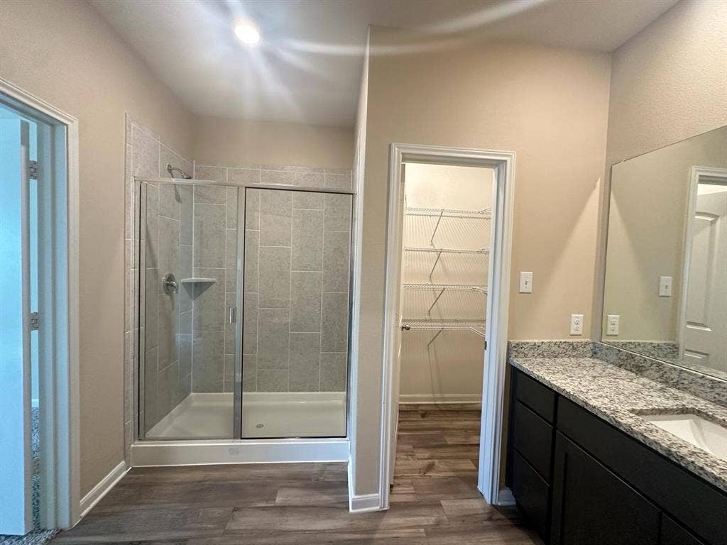 1707 Cotton Blossom Lane, Princeton, TX 75407 Bathroom featuring a glass-enclosed shower with tile surround, a spacious vanity with a speckled countertop and integrated sink, dark wood-finish cabinetry, and wood-finish flooring