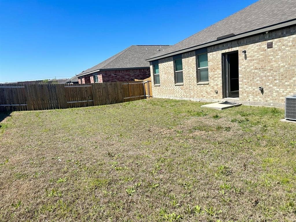 1707 Cotton Blossom Lane, Princeton, TX 75407 Expansive backyard featuring a privacy fence, brick exterior, multiple windows, and a patio door