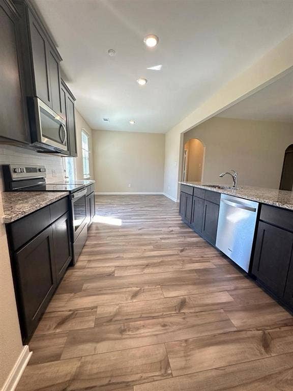 1707 Cotton Blossom Lane, Princeton, TX 75407 Modern kitchen featuring dark cabinetry, stainless steel appliances, speckled stone countertops, and wood-finish flooring