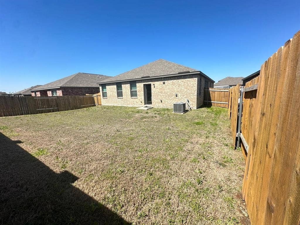 1707 Cotton Blossom Lane, Princeton, TX 75407 Expansive backyard featuring a brick exterior with dark trim, a private wooden fence, and an outdoor HVAC unit
