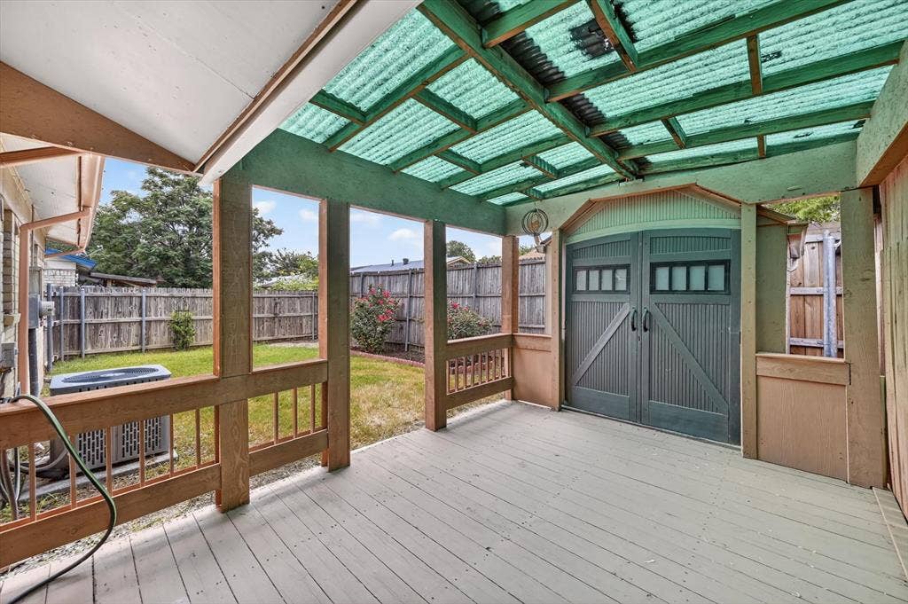 1012 Plover Lane, Arlington, TX 76015 Covered wood-deck patio featuring a corrugated translucent roof, wood railings, and an integrated storage shed with double barn doors