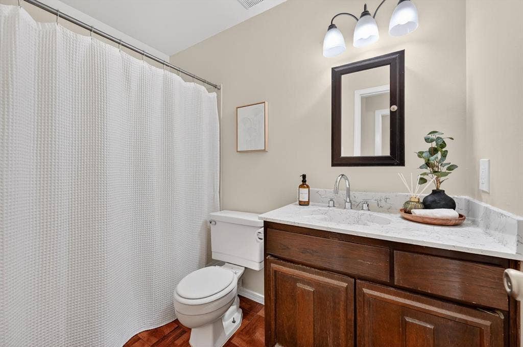 1012 Plover Lane, Arlington, TX 76015 Bathroom featuring a dark wood-finish vanity with a light-colored countertop, chrome faucet, and a wall-mounted mirror