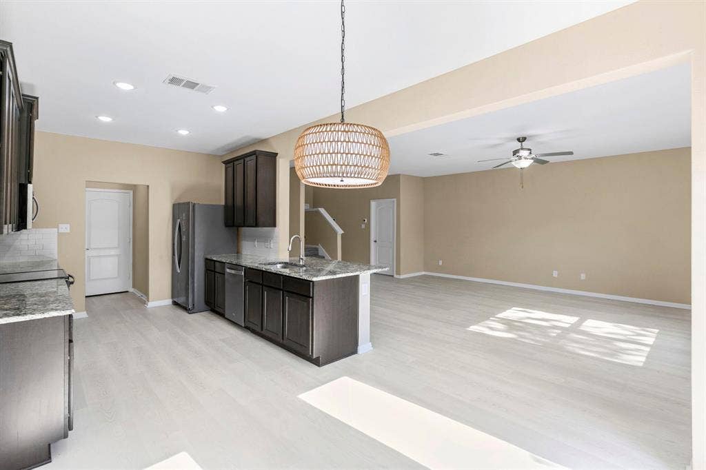 1516 Kinglet Street, DeSoto, TX 75115 Open-concept kitchen featuring dark wood cabinetry, light wood-finish flooring, and a kitchen island with sink