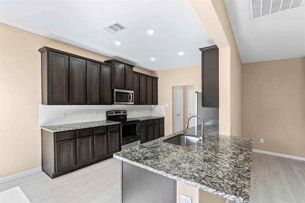 1516 Kinglet Street, DeSoto, TX 75115 Kitchen featuring dark wood cabinetry, light-colored granite countertops, and a subway tile backsplash