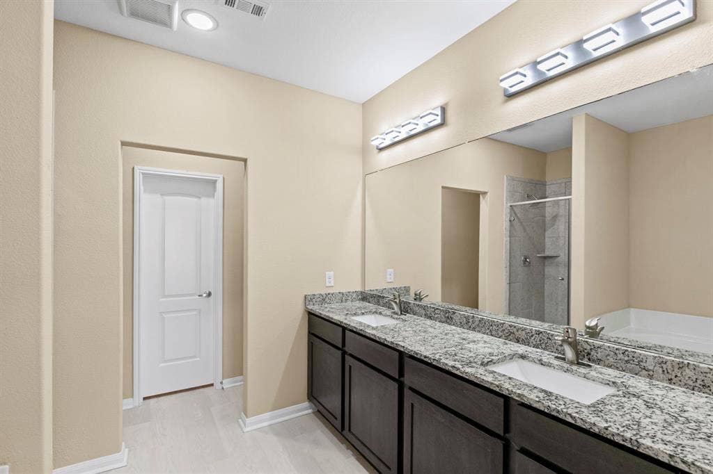 1516 Kinglet Street, DeSoto, TX 75115 Bathroom featuring a double vanity with granite-finish countertops, dark wood-finish cabinetry, and undermount sinks